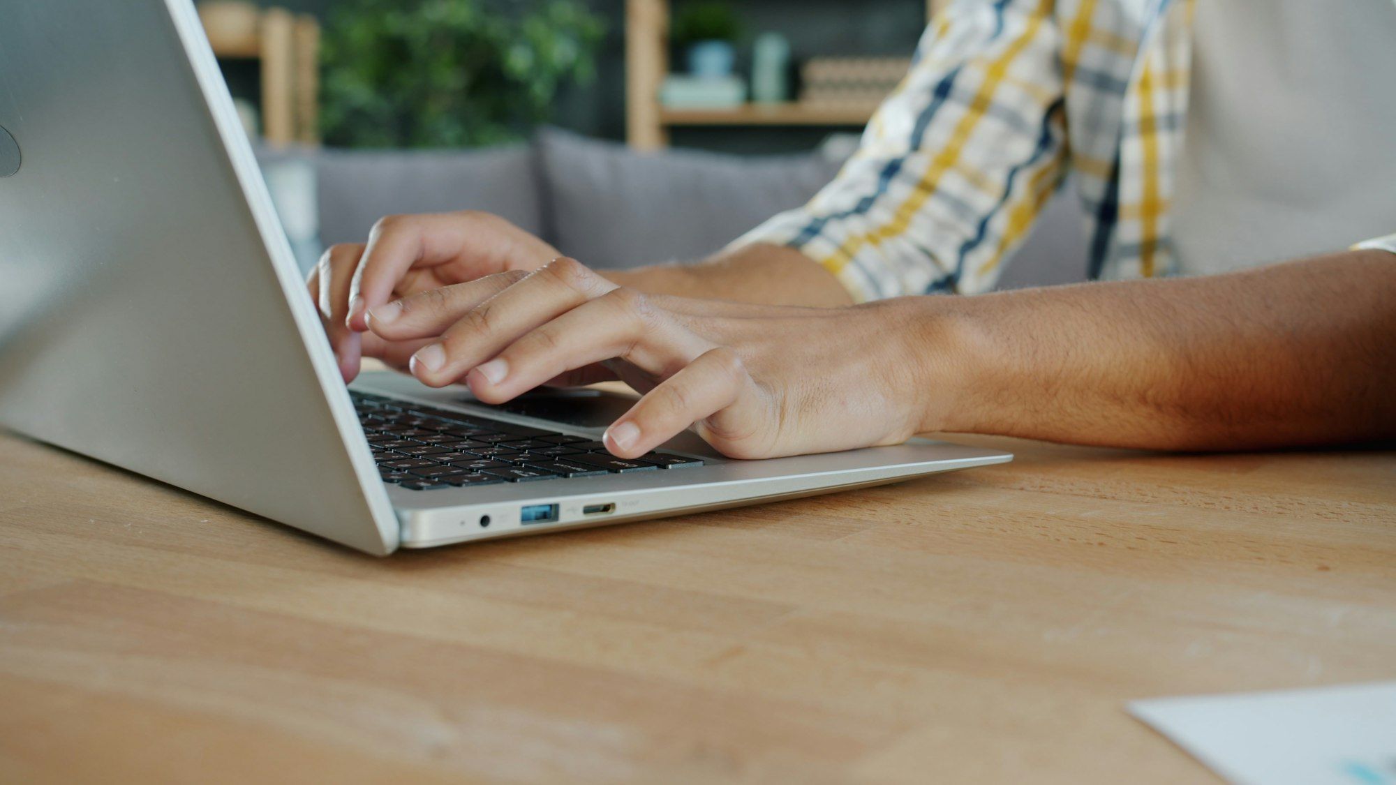 Close-up of hands typing on a laptop keyboard at a wooden desk