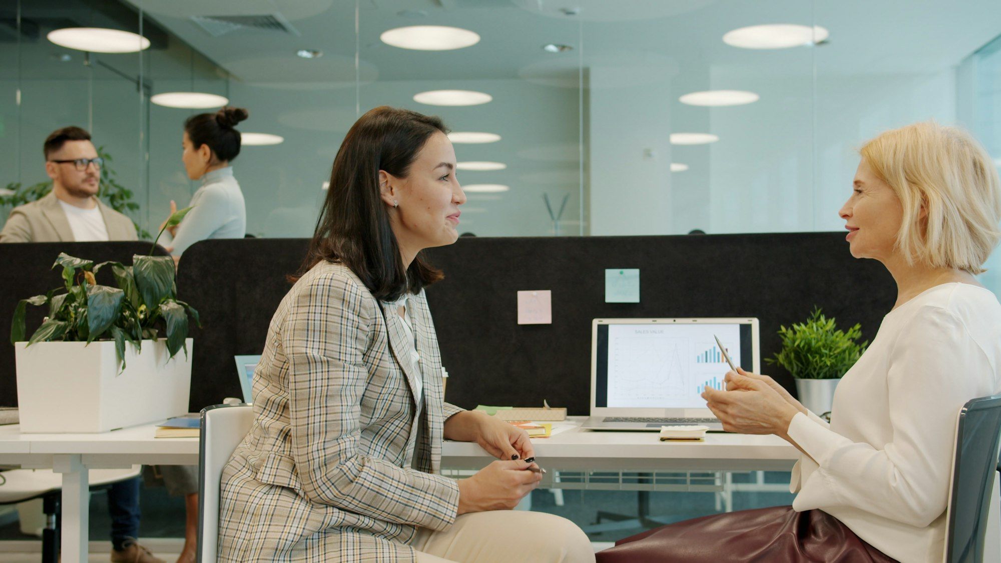 Two colleagues having a focused conversation at a desk, reviewing charts on a laptop in a modern office